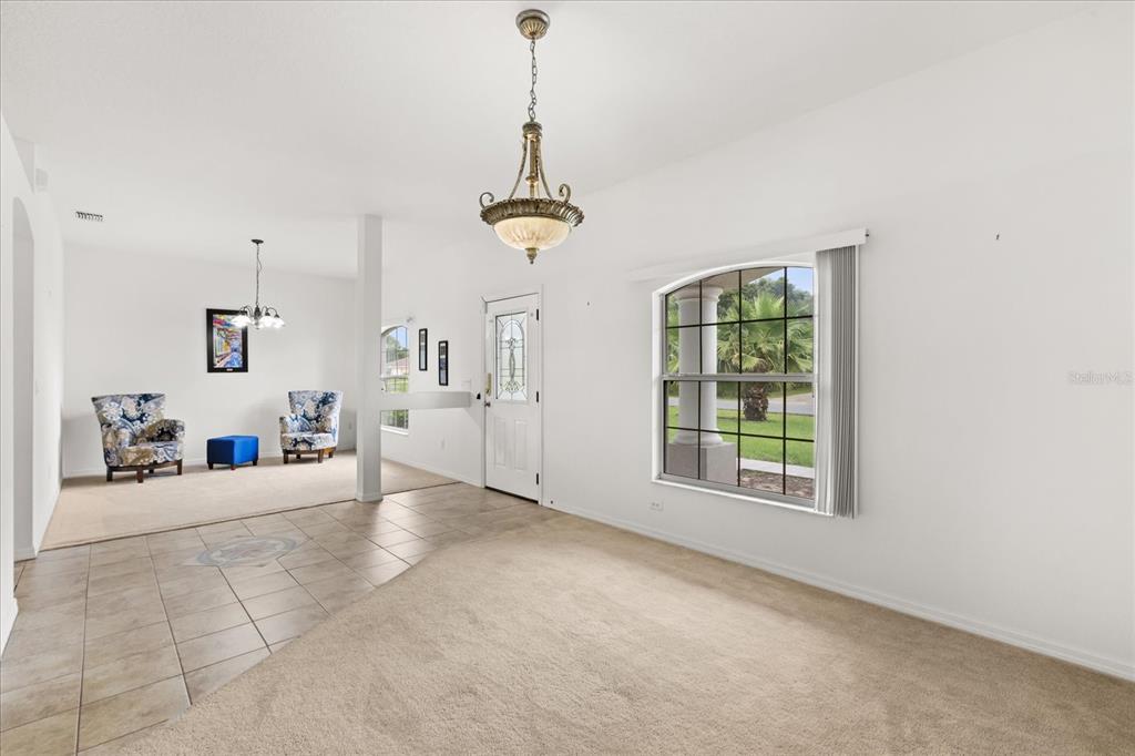 A living room with beige carpet, tile flooring, a chandelier, and a large arched window — 3544 SW 157TH LOOP, OCALA, FL