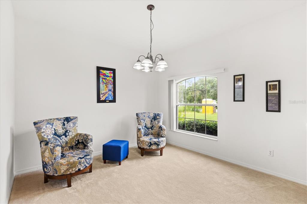 A carpeted room features two patterned armchairs, a blue ottoman, and a chandelier — 3544 SW 157TH LOOP, OCALA, FL