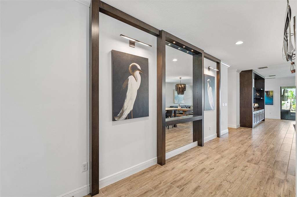 A hallway features wood-look tile flooring, dark wood trim, wall art, and a large mirror — 6658 SYREETA LANE, ST CLOUD, FL