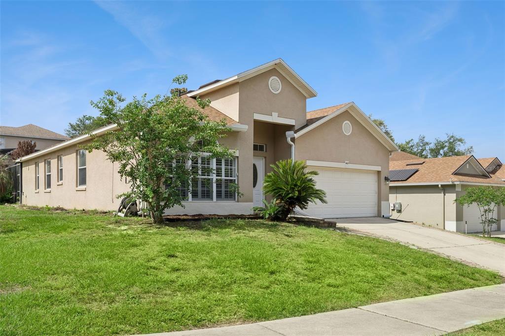 A single-story tan stucco house with a two-car garage and a front lawn — 465 ROB ROY DRIVE, CLERMONT, FL