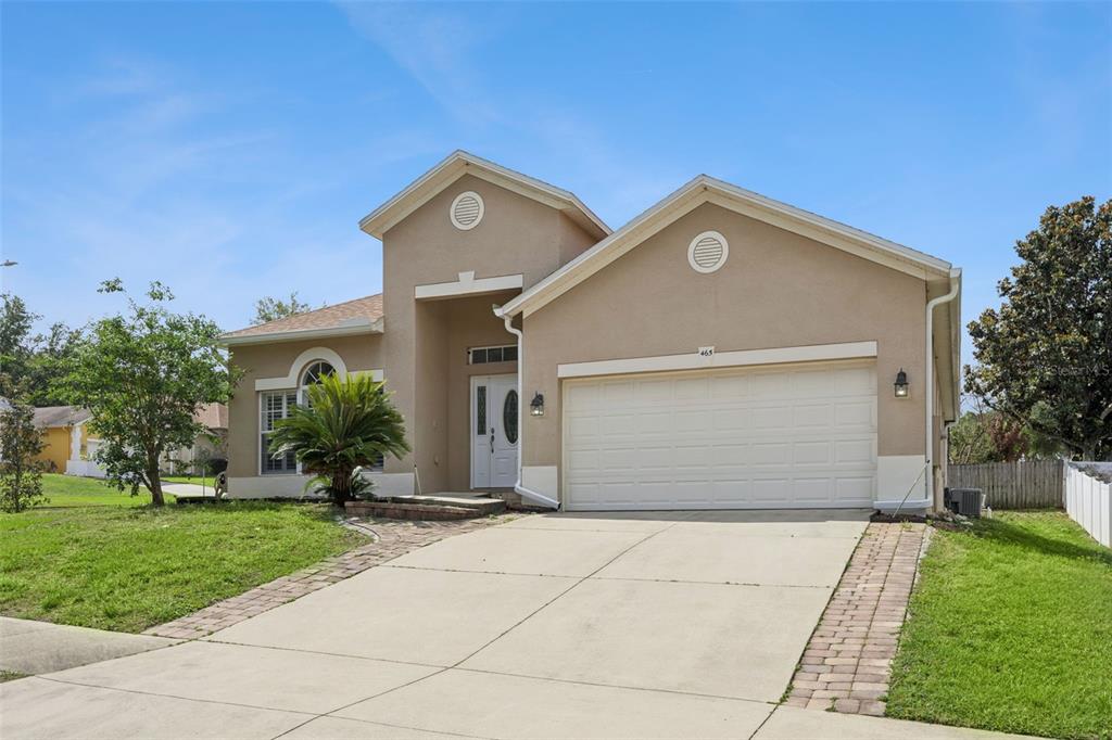 A tan, single-story suburban house with a two-car garage and a paved driveway — 465 ROB ROY DRIVE, CLERMONT, FL