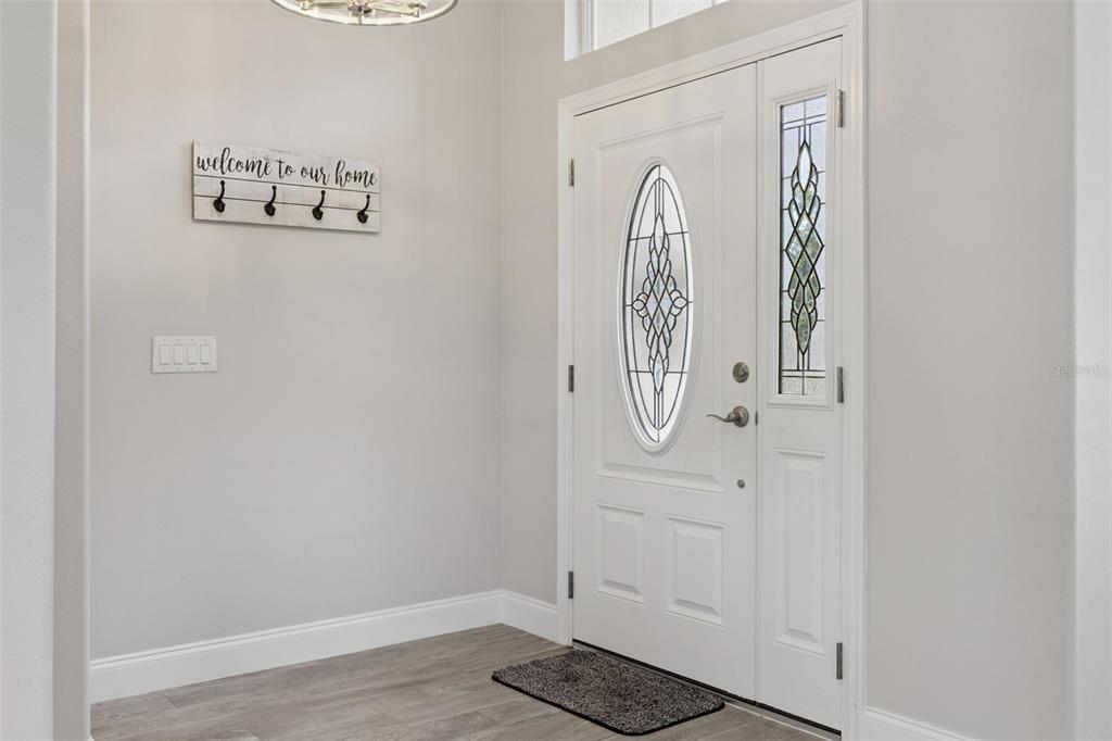 An entryway features light wood-look flooring, a white front door with glass inserts, and wall hooks — 465 ROB ROY DRIVE, CLERMONT, FL