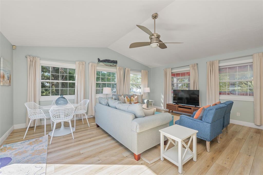 A living room with light blue walls, wood-look flooring, a ceiling fan, and large windows — 287 BOULEVARD DES PINS, ST AUGUSTINE, FL