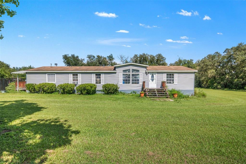 A single-story manufactured home with gray siding sits on a large, grassy lawn — 8512 HAMSTER DRIVE, ZEPHYRHILLS, FL