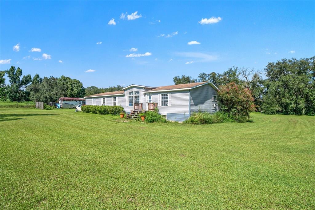 A single-story manufactured home with light gray siding sits on a large, grassy lot — 8512 HAMSTER DRIVE, ZEPHYRHILLS, FL