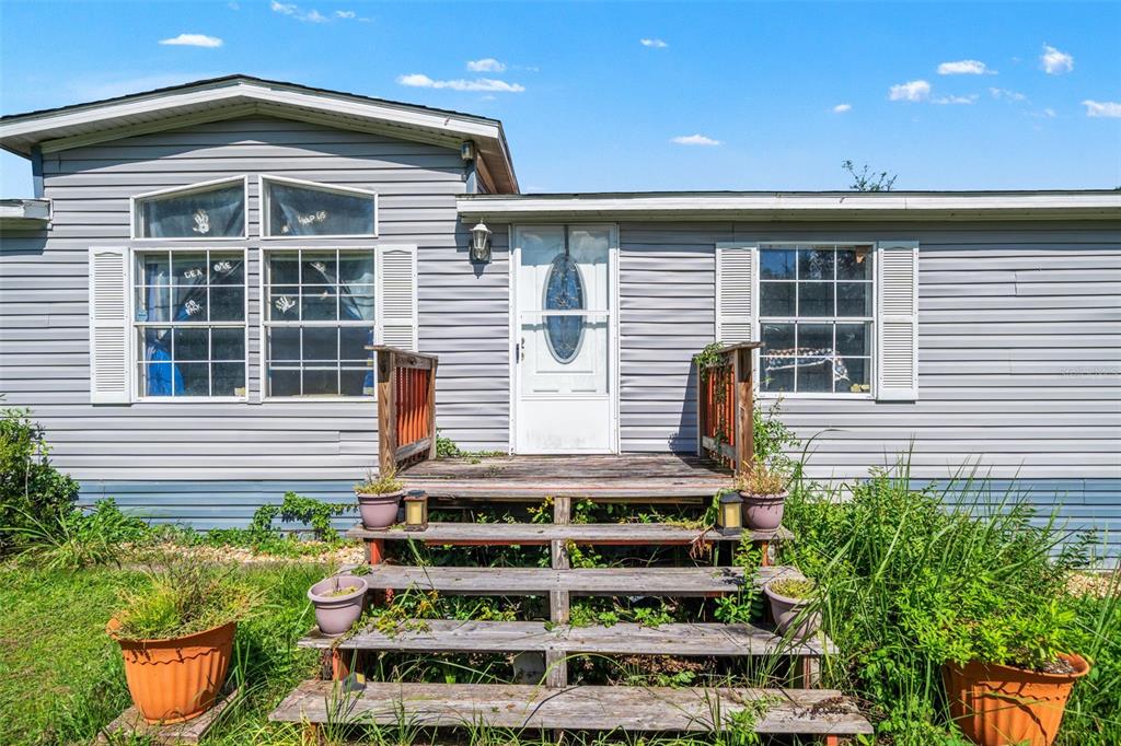 A single-story manufactured home features gray vinyl siding, a wooden front deck, and stairs — 8512 HAMSTER DRIVE, ZEPHYRHILLS, FL