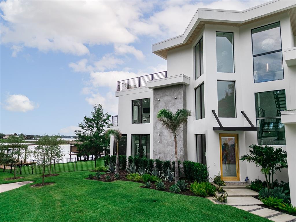 A modern white multi-story house with large windows sits on a grassy lawn near water — 9061 RON DEN LANE, WINDERMERE, FL