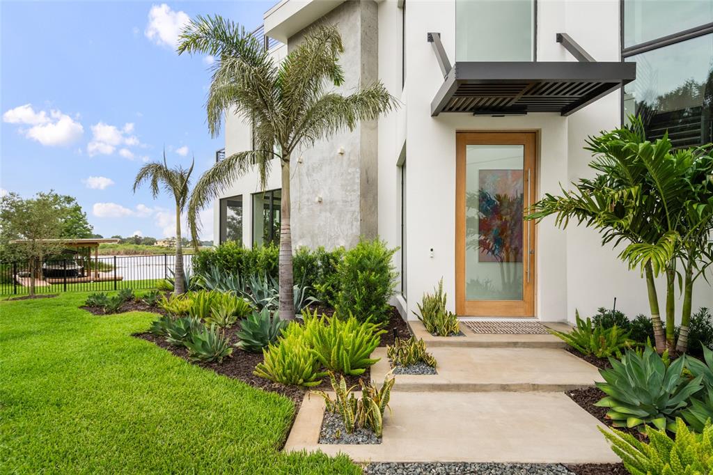 A modern home entrance features a wooden door, concrete steps, and tropical landscaping — 9061 RON DEN LANE, WINDERMERE, FL