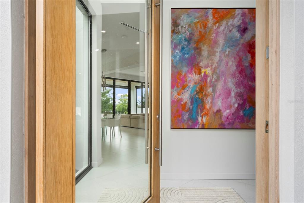 A view through an open wooden door into a bright foyer with abstract wall art — 9061 RON DEN LANE, WINDERMERE, FL