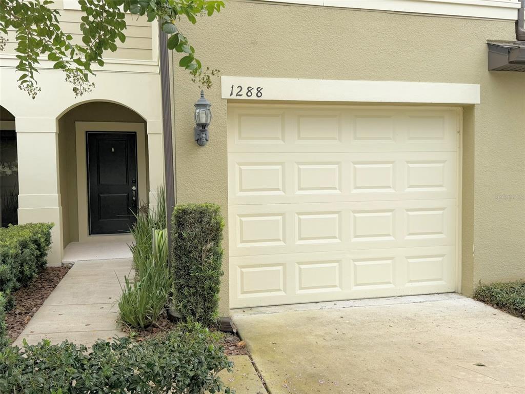 The exterior of a home features a beige garage door, a black front door, and landscaping — 1288 PAVIA DRIVE, APOPKA, FL