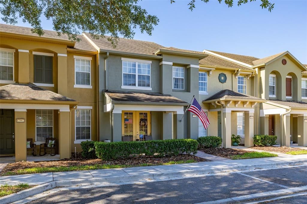 A row of multi-story townhomes with tan and green stucco facades and covered porches — 12966 VENNETTA WAY, WINDERMERE, FL