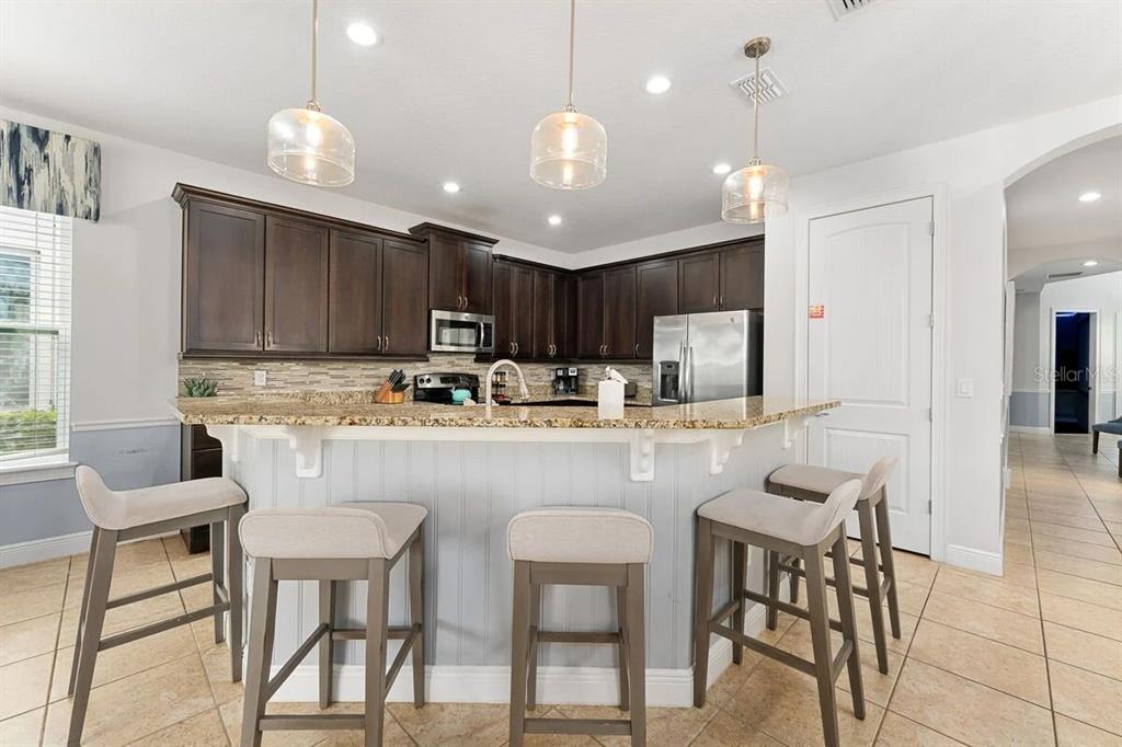 A kitchen features dark wood cabinets, granite countertops, a breakfast bar with stools, and tile flooring — 795 GOLDEN BEAR DRIVE, REUNION, FL