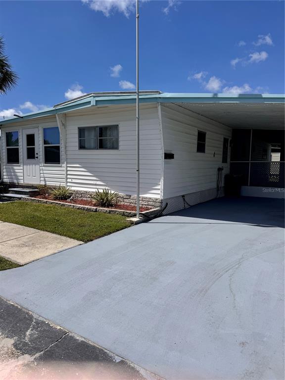 A white mobile home features a carport, a small front lawn, and a flagpole — 6100 62ND AVENUE N UNIT 43, PINELLAS PARK, FL