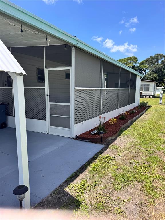 A screened-in porch with a white door sits beside a landscaped garden bed — 6100 62ND AVENUE N UNIT 43, PINELLAS PARK, FL