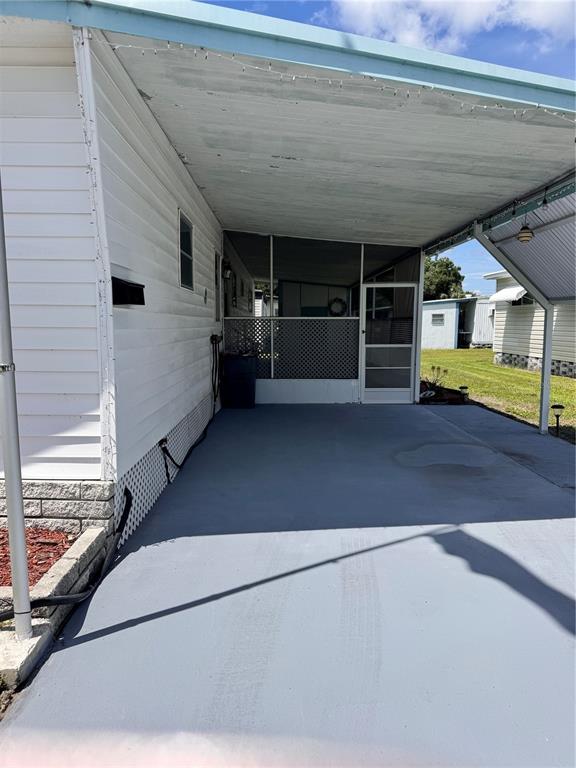 A covered carport with a painted gray concrete floor leads to a screened-in porch area — 6100 62ND AVENUE N UNIT 43, PINELLAS PARK, FL