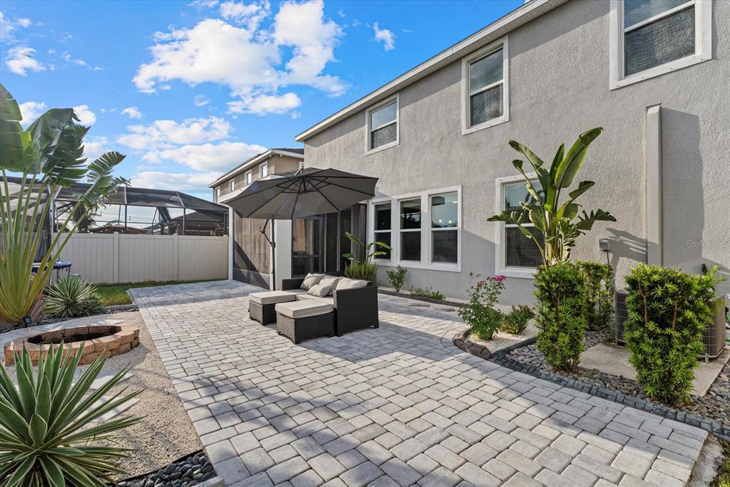 A backyard patio features a paver floor, outdoor seating, an umbrella, and a fire pit — 5030 JACKEL CHASE DRIVE, WIMAUMA, FL