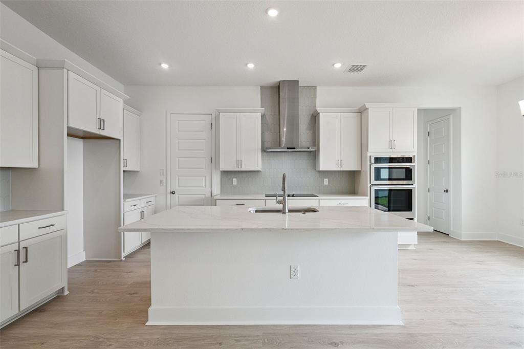 A modern kitchen features a white island, light gray cabinetry, and a white tile backsplash — 17422 HONEYBELL TANGELO COURT, WINTER GARDEN, FL
