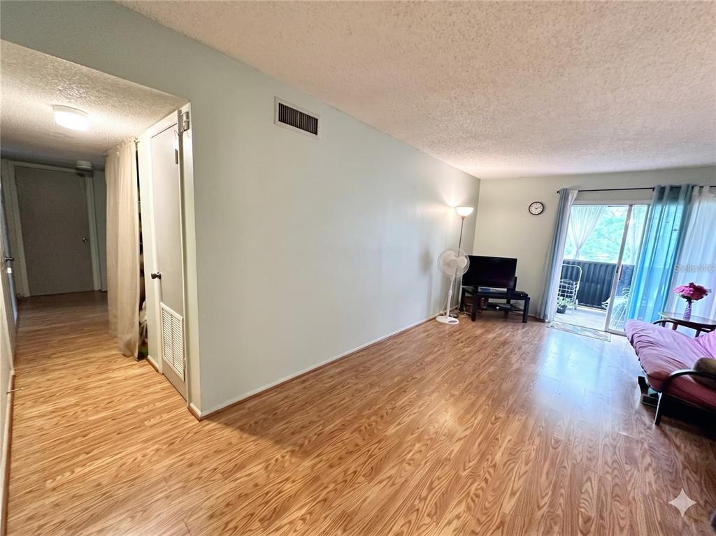 A living room with light wood-look flooring, a sliding glass door, and a futon — 912 LAKE DESTINY ROAD UNIT F, ALTAMONTE SPRINGS, FL