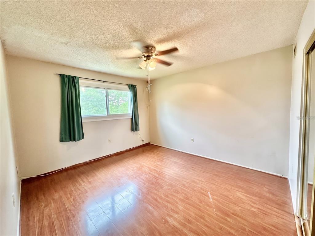 An empty bedroom features wood-look flooring, a ceiling fan, and a window with green curtains — 912 LAKE DESTINY ROAD UNIT F, ALTAMONTE SPRINGS, FL