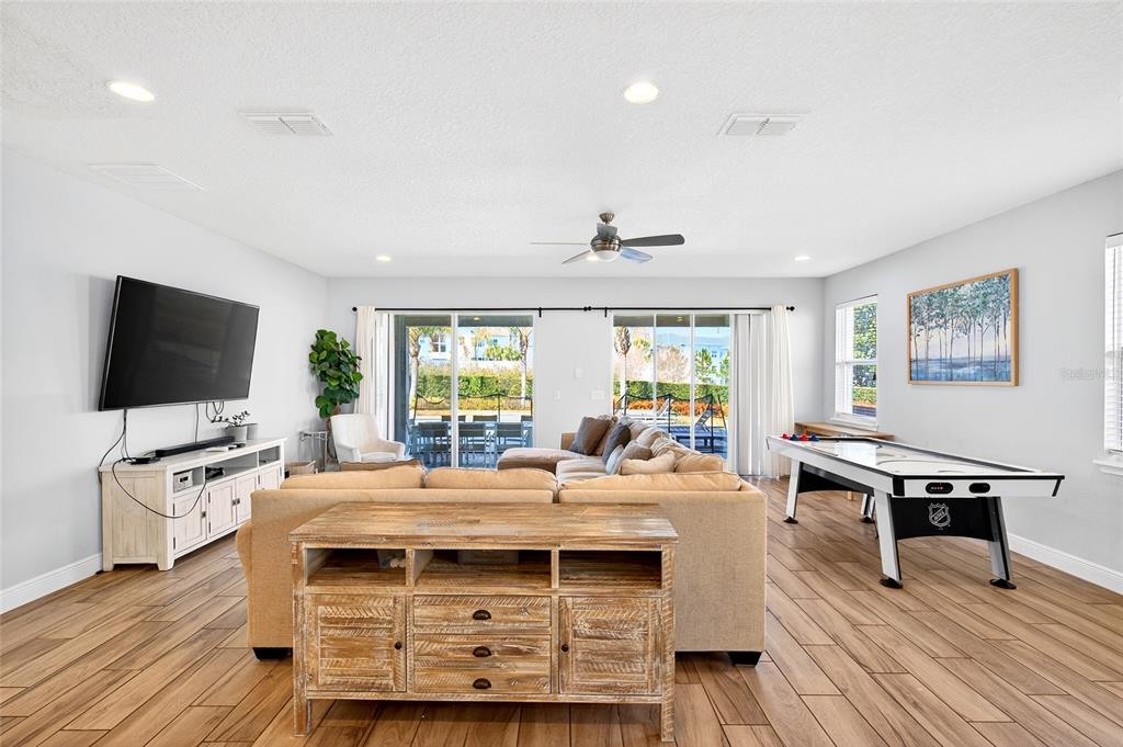 A modern kitchen features white cabinetry, a large island with bar seating, and wood-look flooring — 7724 FAIRFAX DRIVE, KISSIMMEE, FL