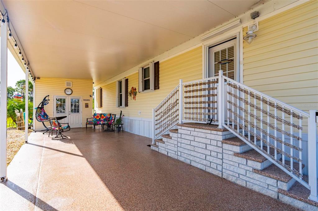 A covered porch with a textured floor, white railings, and outdoor furniture along a yellow house — 1000 KINGS HIGHWAY UNIT 262, PORT CHARLOTTE, FL