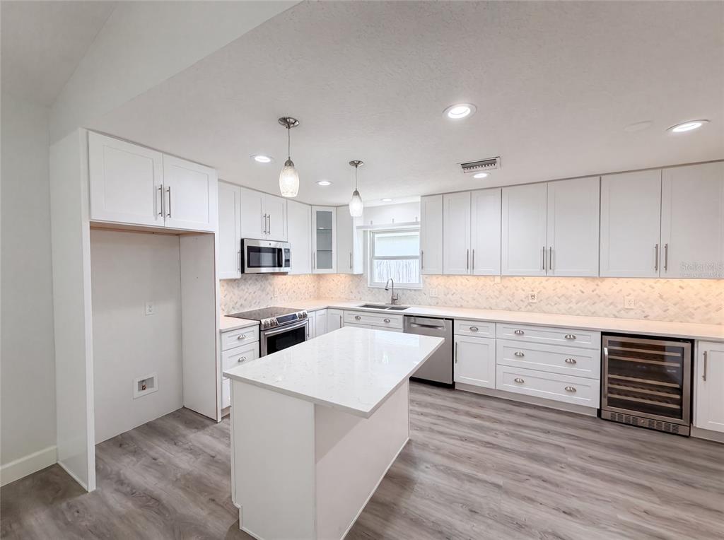 A modern kitchen features white cabinetry, quartz countertops, a center island, and wood-look flooring — 1340 SASSAFRAS AVENUE, ALTAMONTE SPRINGS, FL