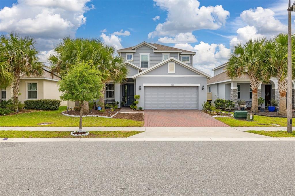A two-story gray house with a brick driveway, a two-car garage, and palm trees — 736 GRAZIE LOOP, DAVENPORT, FL
