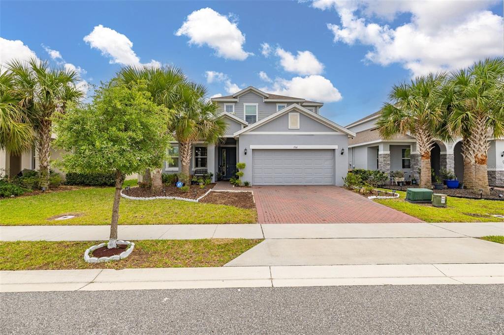 A gray single-story house with a brick driveway, palm trees, and a two-car garage — 736 GRAZIE LOOP, DAVENPORT, FL