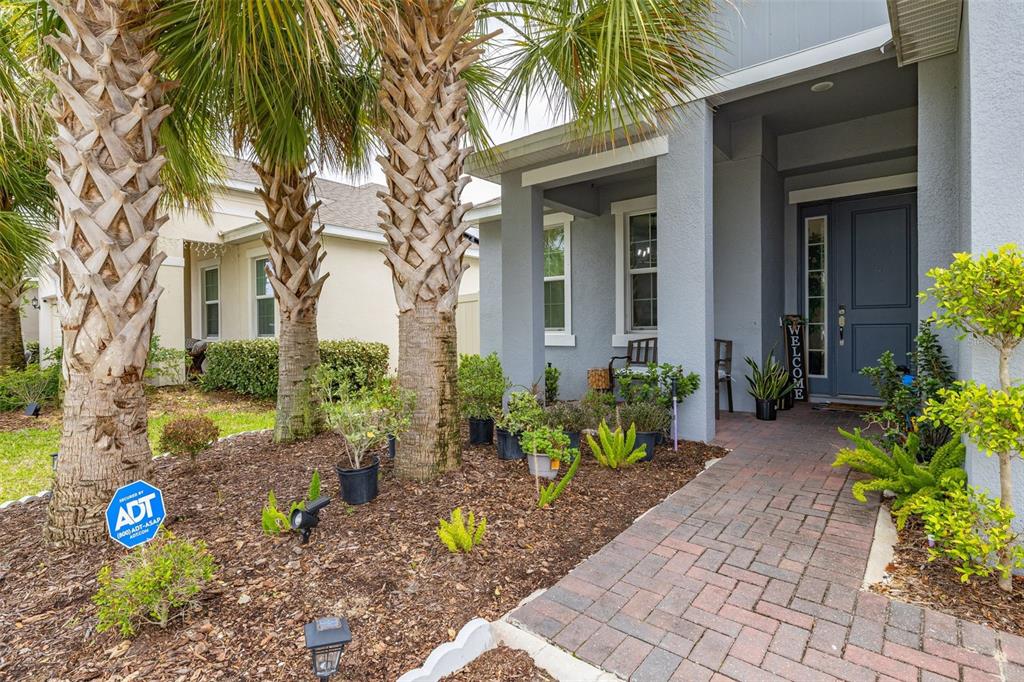 The exterior of a house features a brick walkway, palm trees, and a front porch — 736 GRAZIE LOOP, DAVENPORT, FL