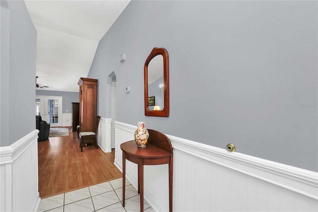 A hallway with white wainscoting, a wooden console table, a mirror, and light-colored tile flooring — 909 ILLINOIS AVENUE, ST CLOUD, FL
