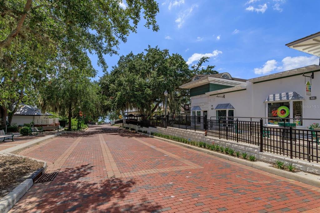 A brick-paved street leads past a white building with a black metal fence — 237 W 4TH AVENUE UNIT 2, MOUNT DORA, FL