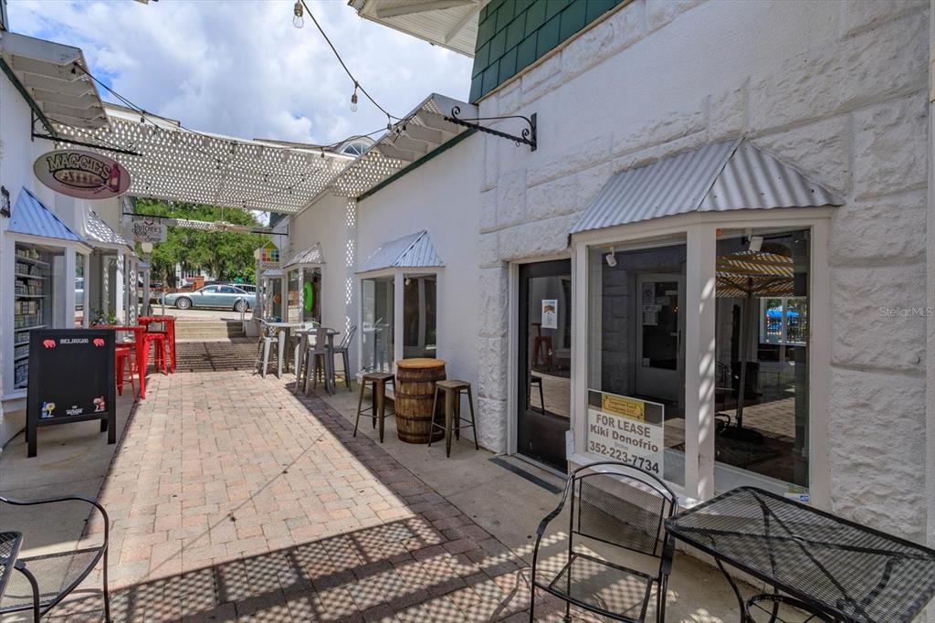 An outdoor brick walkway leads to storefronts with a for lease sign and patio seating — 237 W 4TH AVENUE UNIT 2, MOUNT DORA, FL