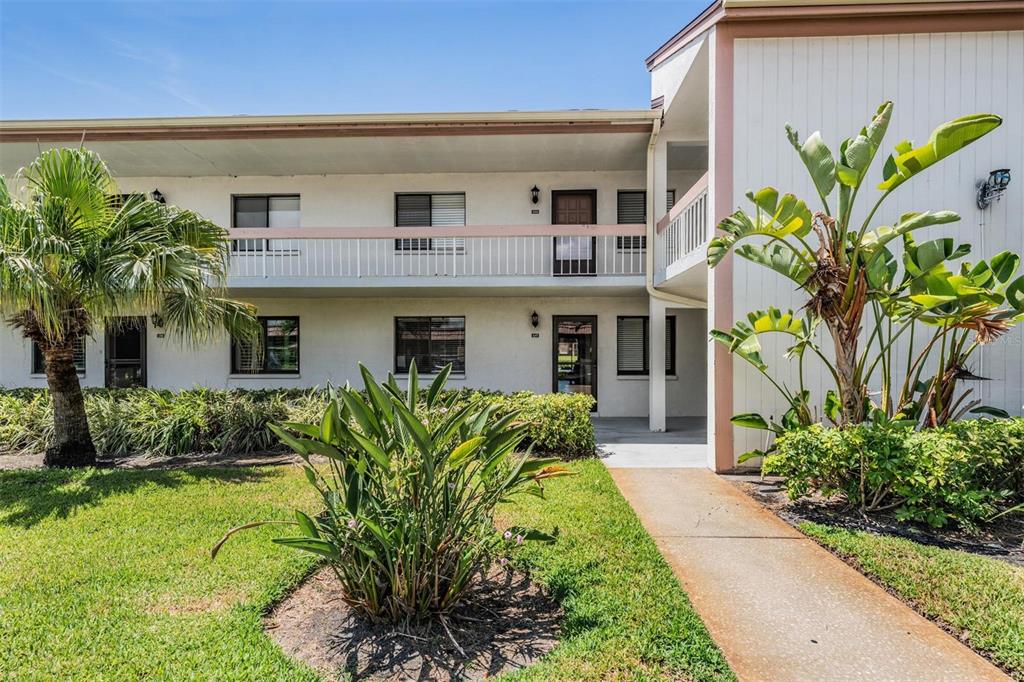 A two-story apartment building exterior features white stucco walls, a walkway, and tropical landscaping — 107 LAKEVIEW PLACE UNIT 7, OLDSMAR, FL