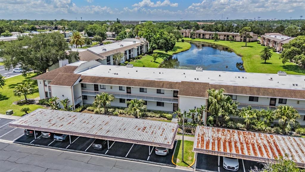 An aerial view shows a multi-story apartment building with carports and a nearby pond — 107 LAKEVIEW PLACE UNIT 7, OLDSMAR, FL