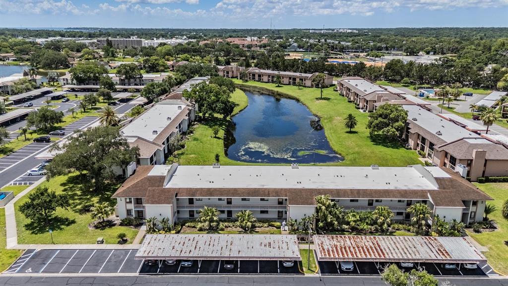 An aerial view shows apartment buildings surrounding a central pond with covered parking areas below — 107 LAKEVIEW PLACE UNIT 7, OLDSMAR, FL