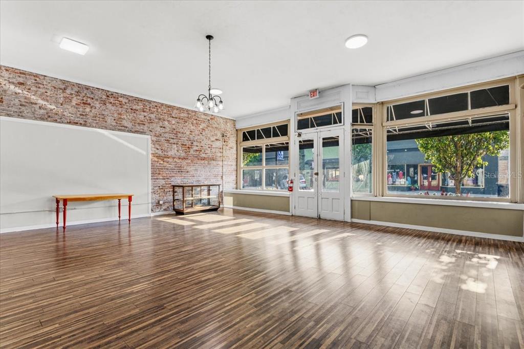An empty commercial space features wood-look flooring, a brick accent wall, and large storefront windows — 14827 MAIN STREET, ALACHUA, FL