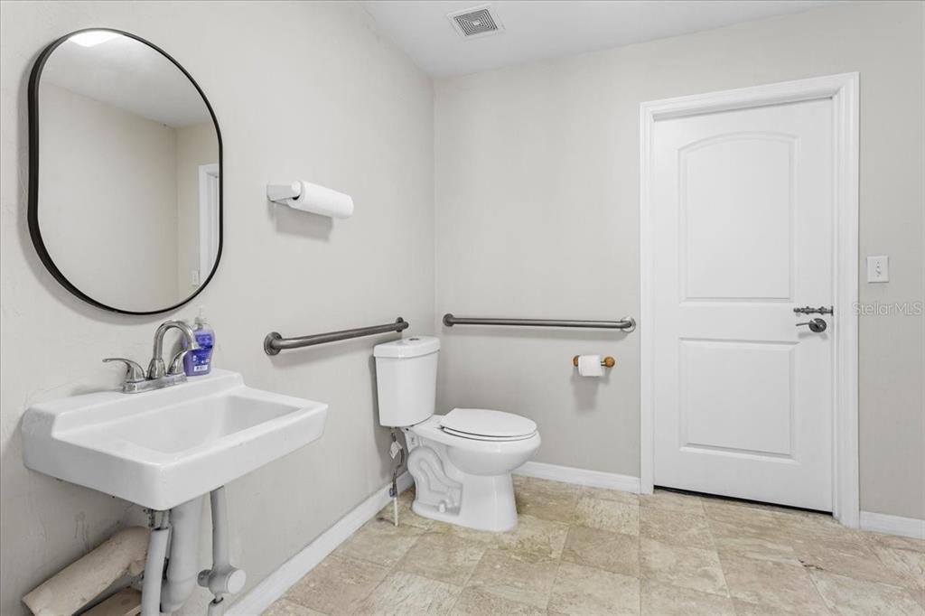 A bathroom features a wall-mounted sink, a toilet with grab bars, and light-colored tile flooring — 14827 MAIN STREET, ALACHUA, FL