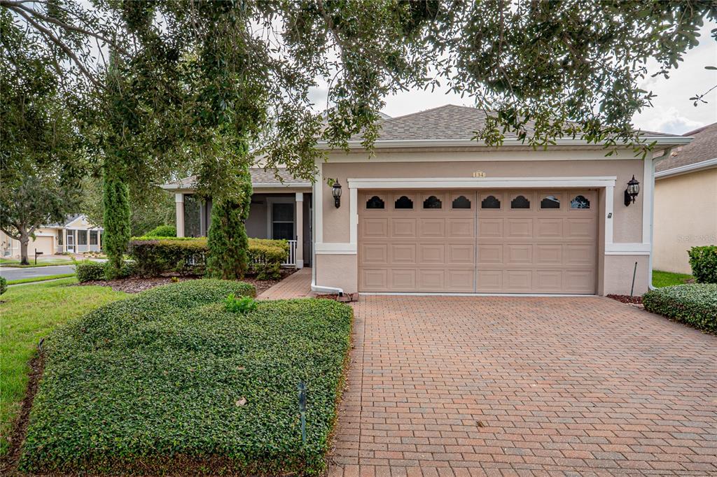 A single-story house with a beige stucco exterior, a two-car garage, and a brick driveway — 134 FLAME VINE WAY, GROVELAND, FL