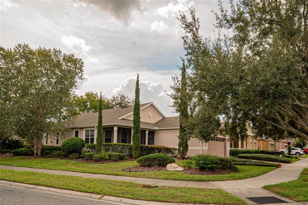 A single-story house with a tan exterior, a screened porch, and tall cypress trees — 134 FLAME VINE WAY, GROVELAND, FL
