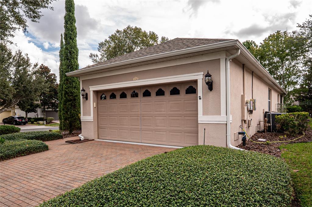 A beige detached garage with a two-car door and a brick paver driveway — 134 FLAME VINE WAY, GROVELAND, FL
