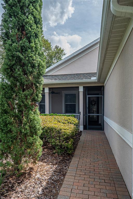 A brick walkway leads to a screened-in porch beside a tall evergreen tree — 134 FLAME VINE WAY, GROVELAND, FL