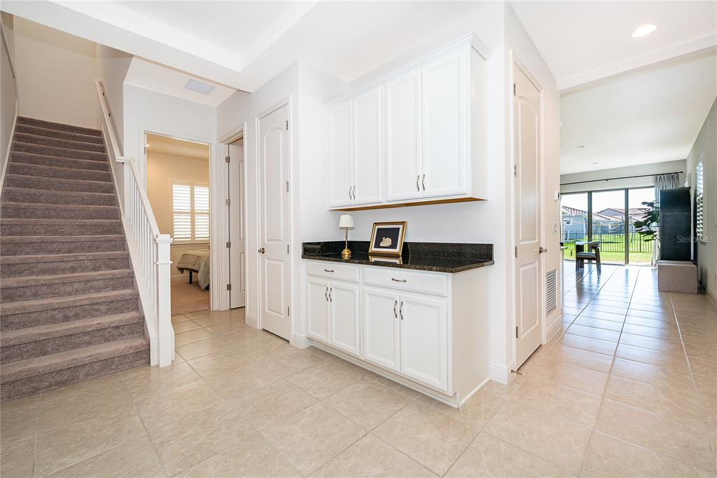 A foyer with a carpeted staircase, white cabinetry, a dark countertop, and tiled flooring — 8124 MABURY LANE, ORLANDO, FL