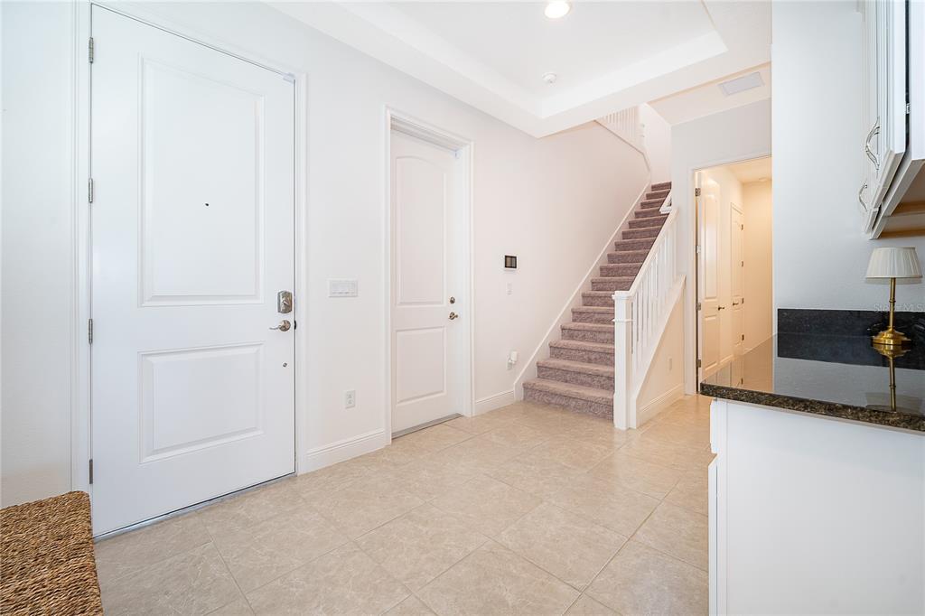 A bright entryway features tile flooring, a white front door, and stairs with carpeted steps — 8124 MABURY LANE, ORLANDO, FL