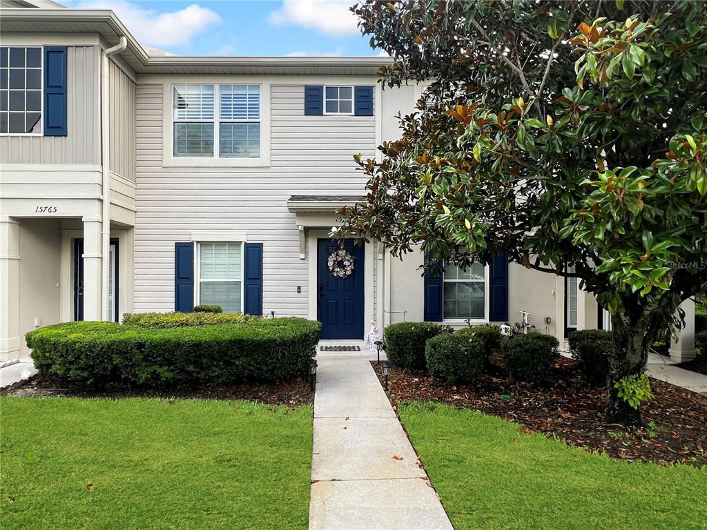 A two-story townhouse exterior features light siding, blue shutters, a front door, and landscaping — 15767 STABLE RUN DRIVE, SPRING HILL, FL