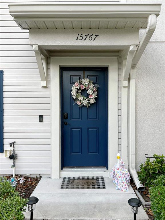 A blue front door with a floral wreath sits under a covered entryway — 15767 STABLE RUN DRIVE, SPRING HILL, FL