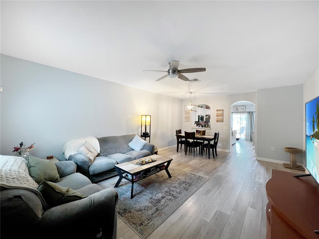 A living room with light wood-look flooring, a gray sofa, and an adjacent dining area — 15767 STABLE RUN DRIVE, SPRING HILL, FL