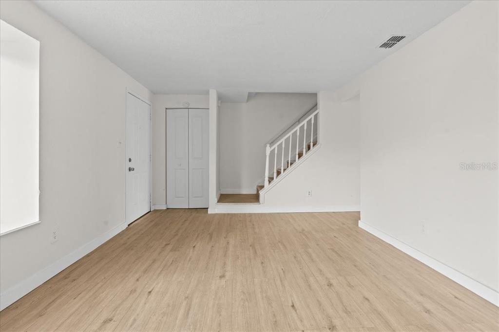 An empty room with light wood-look flooring, white walls, a staircase, and a closet door — 4945 SANOMA VILLAGE UNIT B, ORLANDO, FL