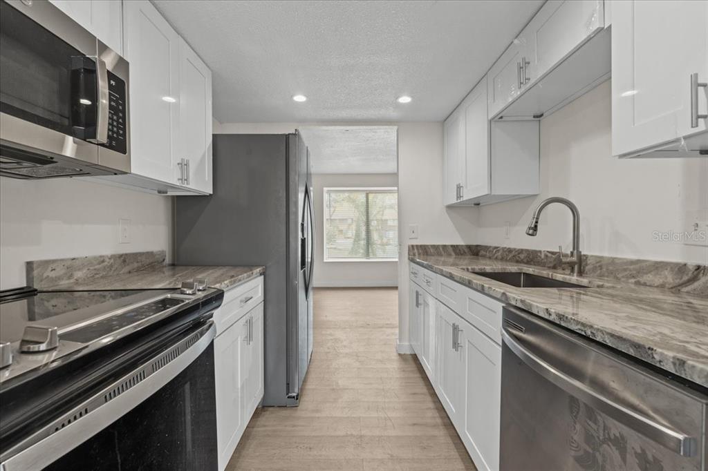 A galley kitchen features white cabinets, granite countertops, and stainless steel appliances — 4945 SANOMA VILLAGE UNIT B, ORLANDO, FL