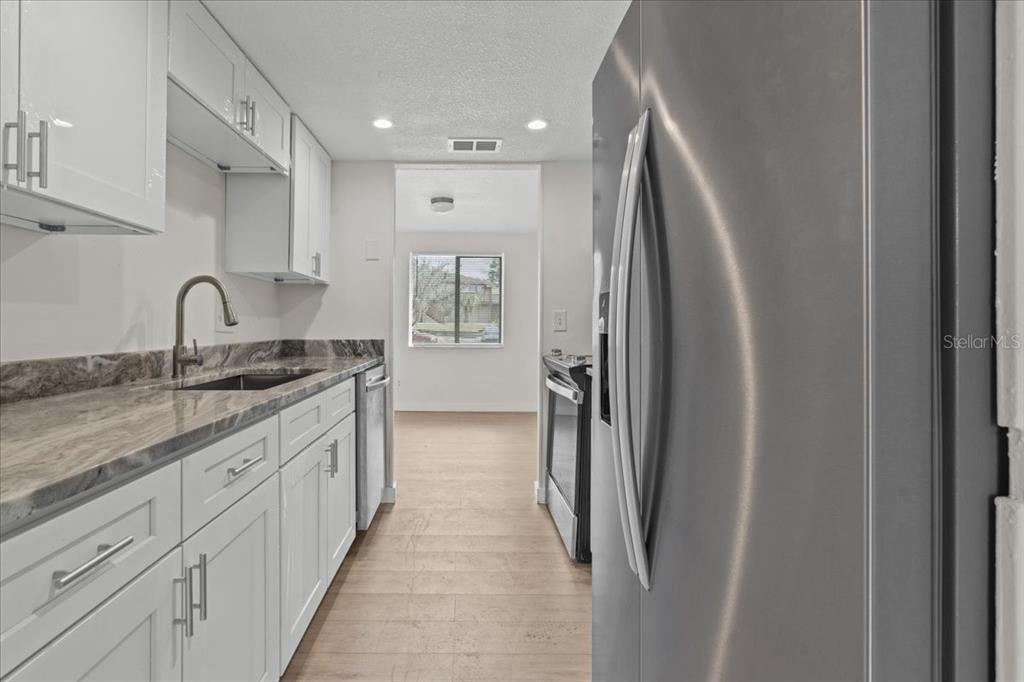 A galley kitchen features white cabinets, stone countertops, stainless steel appliances, and wood-look flooring — 4945 SANOMA VILLAGE UNIT B, ORLANDO, FL