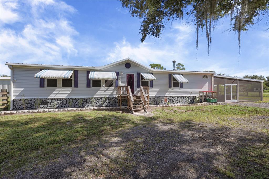 A single-story manufactured home with light siding, stone skirting, and a screened-in porch — 4480 FORT SIMMONS AVENUE, LABELLE, FL